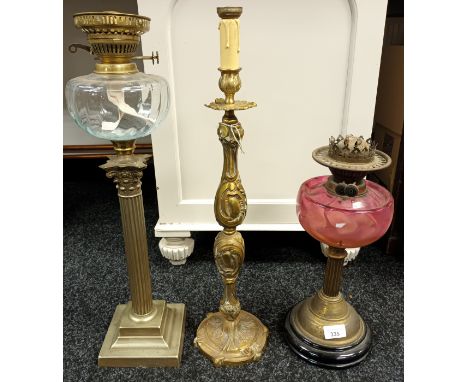 Two antique paraffin lamps together with an ornate candle stick. Corinthian column and clear glass paraffin lamp. Cranberry g