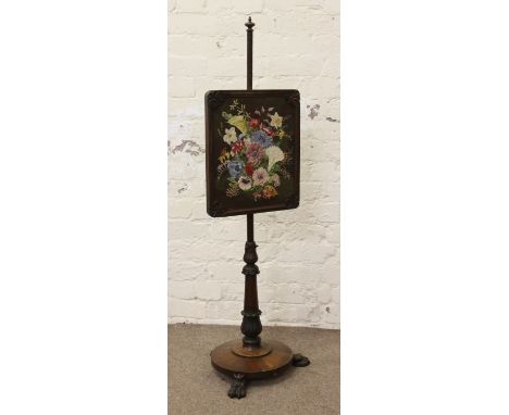 A Victorian carved rosewood pole screen with floral woolwork panel and raised on carved paw feet.