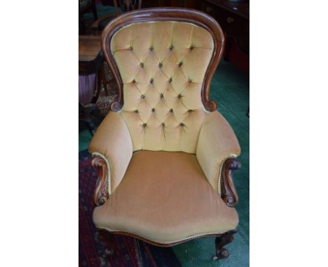 A Victorian mahogany spoon back armchair, stuffed over deep buttoned upholstery, carved scroll arms, cabriole legs, ceramic c