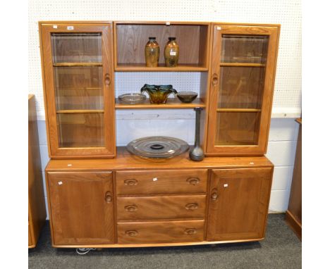An Ercol sideboard, central shelving flanked by glazed cupboards, above three long drawers, flanked by cupboards, caster feet