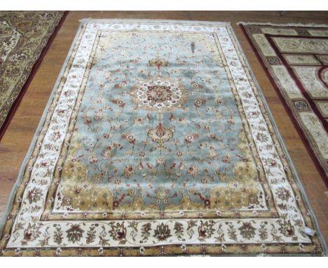 A WOOL RUG the light blue and beige ground with central floral panel within a conforming border 233cm x 153cm 