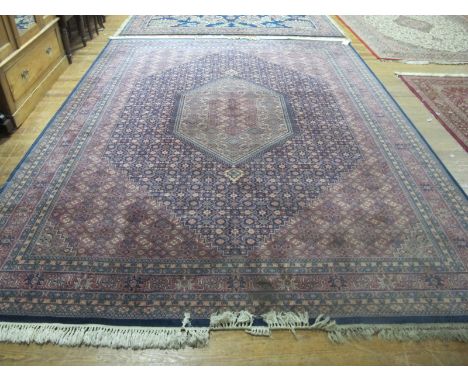 A WOOL RUG the light pink and indigo ground with central floral panel within a conforming border 358cm x 275cm
