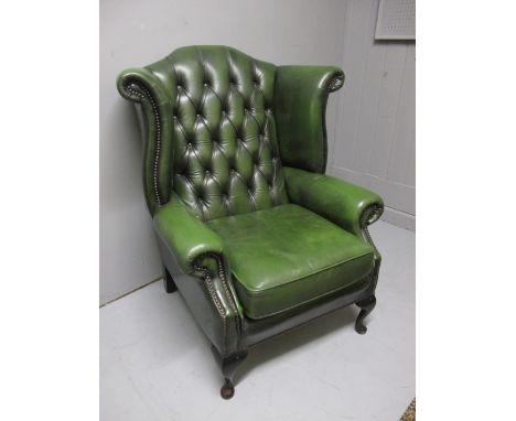 A GREEN HIDE UPHOLSTERED LIBRARY WING CHAIR with deep button upholstered back and seat with loose cushion on cabriole legs wi