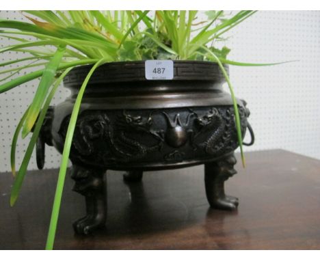 AN ORIENTAL BRONZE PLANTER of circular form the frieze moulded in high relief with dragons and mask carrying handles raised o
