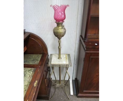 A VICTORIAN BRASS FLOOR STANDARD OIL LAMP with ruby glass shade above an embossed resevoir on spiral twist column with oynx t