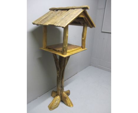 A RUSTIC GARDEN BIRD HOUSE the slatted pitched roof above an open shelf raised on a rustic base 154cm (h) x 64cm (w) x 48cm (