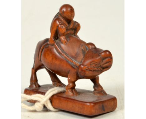 A Japanese wood netsuke of a youth seated upon an ox, on rectangular base, late Edo, length 3.6cm, height 4.2cm.