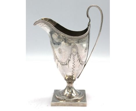 A George III silver helmet shaped cream jug, beaded rim with engraved foliate banner decoration, upon square shaped base, hal
