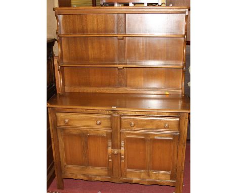 An Ercol mid-elm 'Golden Dawn' kitchen dresser, having a two-tier open plate rack over base fitted with twin frieze drawers o