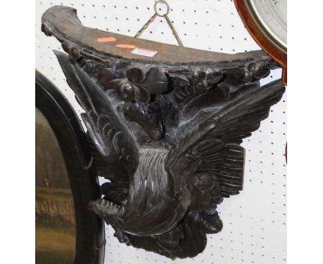 An early 20th century Continental carved and ebonised oak demi-lune wall bracket, modelled as an eagle with goat, 48 x 38cm