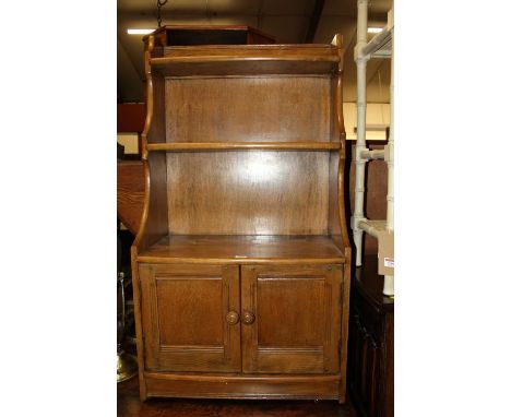 An Ercol mid-elm narrow waterfall bookshelf, having twin lower cupboard doors, w.61cmW: 61cm, H: 114cm, D: 33cm