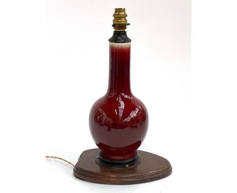 A porcelain red glazed sang de boeuf vase of bottle dorm, converted to a lamp, on a wooden base, the vase 27.5cmH