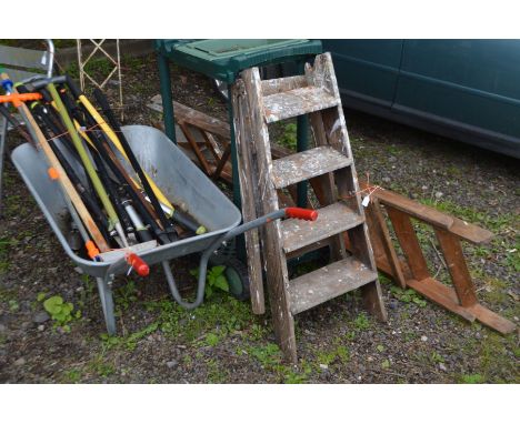 A GALVANISED WHEELBARROW, containing a collection of garden hand tools, two wooden step ladders and a plastic garden trolley 