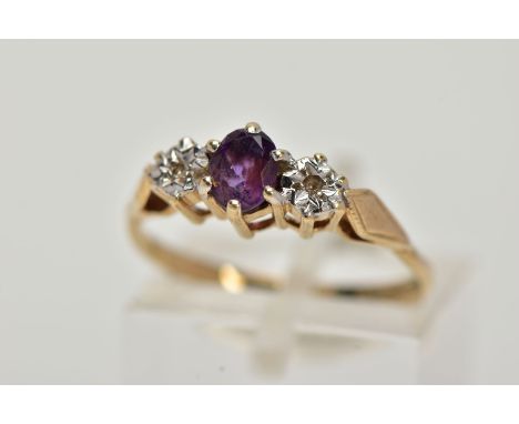 A 9CT GOLD THREE STONE RING, centring on a claw set, oval cut amethyst, flanked with illusion set single cut diamonds, textur