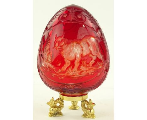 A ruby overlay glass Russian egg, Faberge label under base on swan design gilt metal stand, height 11cm.