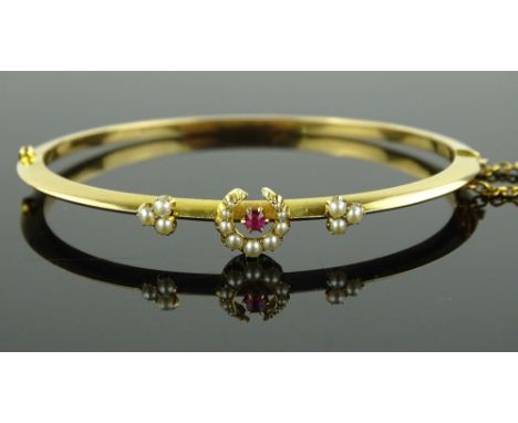 An Edwardian unmarked gold seed pearl and ruby set hinged bangle, 7.7g.