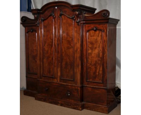 A Victorian mahogany four door wardrobe, the flared arched cornice above a pair of panel doors enclosing slides, raised on ba