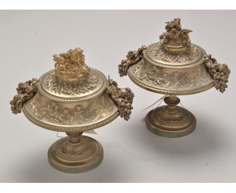 A pair of early 20th Century brass garnitures, the covers with floral pattern finials, flanked by ribbon tied cornucopia hand