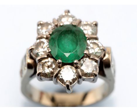 An emerald and diamond cluster ring, the oval facet cut emerald measuring 8.3 x 7.5 x 5mm, estimated to weigh approximately 1