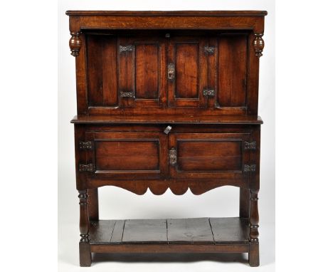 A 17th Century and later oak livery cupboard, the plain cornice with turned drops above a pair of panel doors enclosing a sin