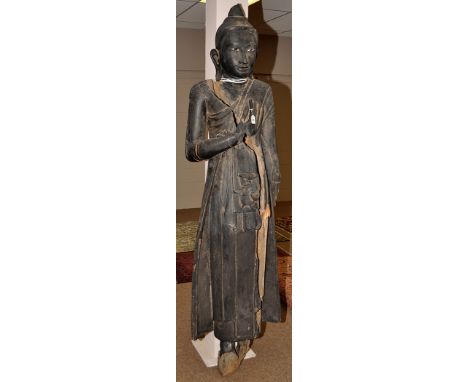 A large early 20th Century carved and ebonised teak  Buddha,standing with right hand covering heart, mother-of-pearl inset ey