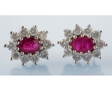 A pair of ruby and diamond cluster earrings, each set with oval facet cut ruby surrounded by ten brilliant cut diamonds, in 1