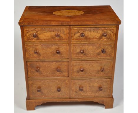 An early 20th Century figured walnut chest of eight short drawers with turned wooden handles, the top with inlaid oval panel 