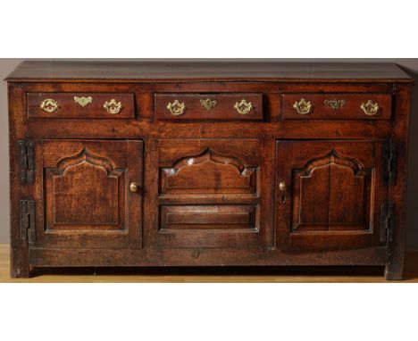 An 18th Century oak dresser base, fitted three frieze drawers with brass handles, above a pair of arched bevelled panel doors