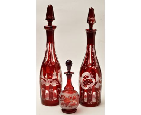 Two slender Bohemian ruby overlaid glass decanters and stoppers, engraved, leaping stags and buildings amongst trees, the tal