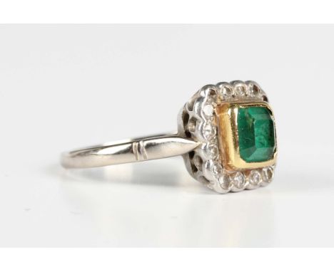 A two colour gold, emerald and diamond square cluster ring, collet set with the cut cornered square cut emerald within a surr