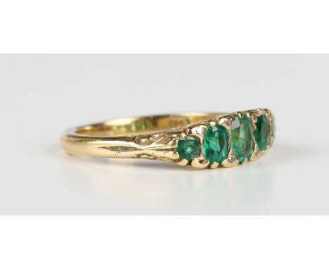 An 18ct gold, emerald and diamond ring, mounted with a row of five graduated emeralds with four pairs of diamond points at in