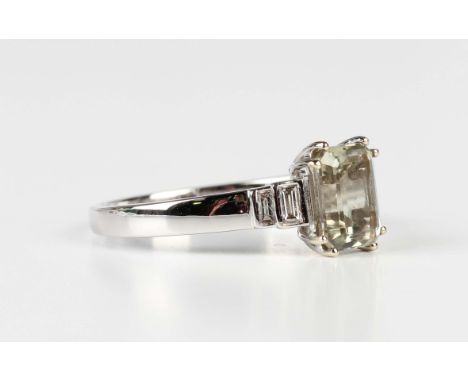 An 18ct white gold ring, mounted with a rectangular step cut csarite between baguette cut diamond two stone shoulders, Birmin