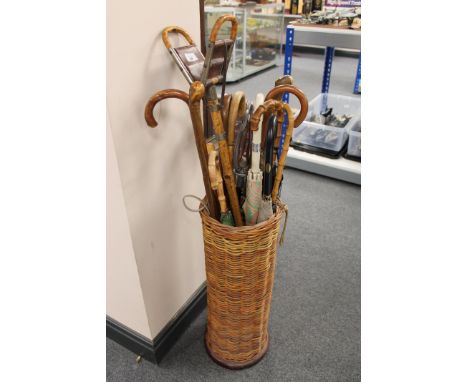 A wicker cylindrical stick stand, containing a quantity of umbrellas, two shooting sticks, walking canes, etc. 