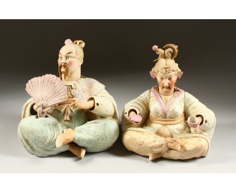 A PAIR OF 19TH CENTURY BISQUE PORCELAIN SEATED "NODDING" FIGURES of a man holding a fan and a lady holding a cup and saucer. 