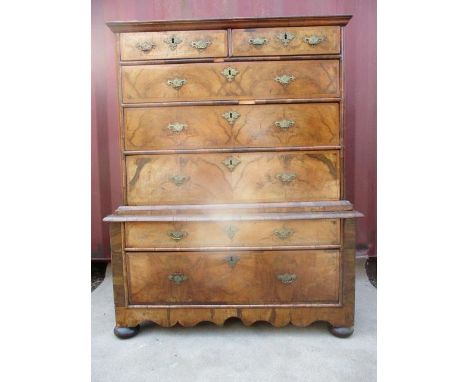 An early 18th century walnut chest on stand having a quarter veneered, crossbanded top over two short and three long drawers,