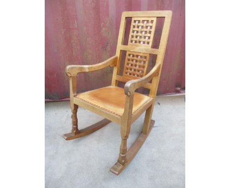 A Robert Thompson Mouseman oak rocking chair with a carved, woven effect back, curved arms and brown leather upholstered seat