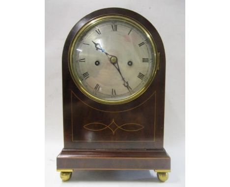 An Edwardian mahogany, string inlaid, arched topped mantle clock having a silvered dial with Roman numerals, lion ring handle