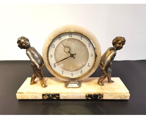 An Art Deco marble mantel clock, the face having stylised brass numerals and being held aloft by two spelter children on a st