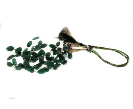 An Indian emerald three strand necklace,  the lozenge shaped stones silk threaded, to a braided silk tie 