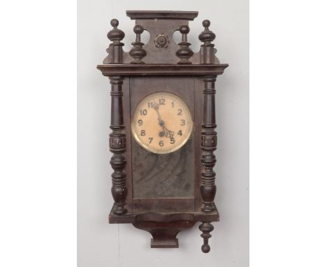 A wooden cased wall clock with pendulum, with carved wooden plinth and finial decoration. Comes with key. H:57cm, W: 29cm.  C