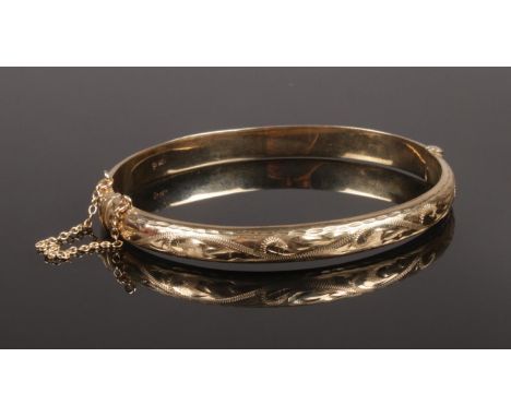 A 9ct gold bangle. With engraved decoration and safety chain. 8.63g.  