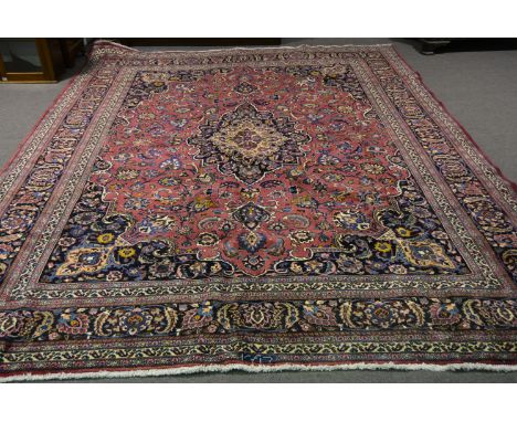 A Meshed carpet, central floral medallion against a burgundy ground with scrolling palmette design, enclosed by spandrels, an
