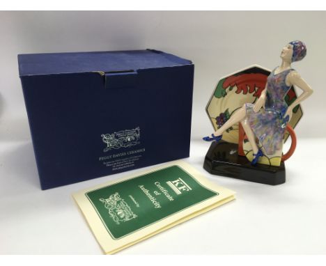 A boxed Peggy Davies ceramic figure of an Art Deco maiden seated amongst Clarice Cliff style items, sculpted by Kevin Francis