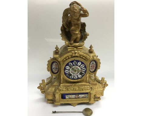 A giltwork 8 day mantle clock with painted porcelain panels of flowers and cherubs and surmounted by a figure of a cherub, ap