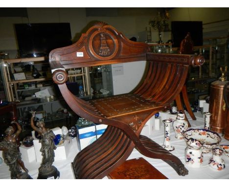 A vintage 'X' frame chair displaying a family crest and monogram on the back rest
