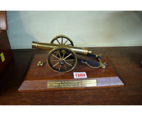 A brass desk canon, the mahogany plinth with brass plaque inscribed 'To H Butterworth Esq., made and presented by apprentices