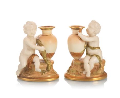 PAIR OF ROYAL WORCESTER SPILL VASES, CODE FOR 1928 each modelled as a putto holding an urn, in blush ivory and lustrous tones