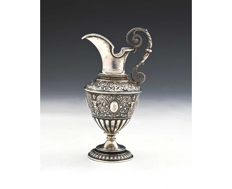 A Continental silver-coloured metal ewer or jug, modelled in the classical form, the body decorated in relief with foliage an