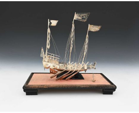 A Chinese silver-coloured metal model of a sailing ship or a junk, ensuite with rigging and sails, with a glazed cover and wo