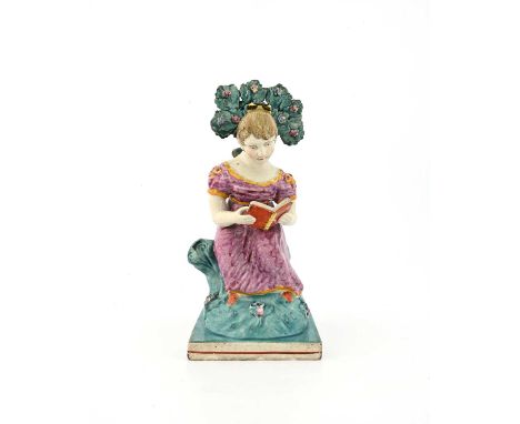 An Obadiah Sherratt Staffordshire figure of a girl reading, circa 1820, sitting on a tuffet with boccage tree, square base, 2